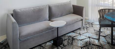 A grey sofa with a round white side table, a patterned rug, and a chair with a blue cushion.
