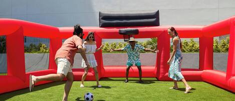 Un grupo de personas jugando fútbol en un campo cubierto de césped con un obstáculo inflable rojo.