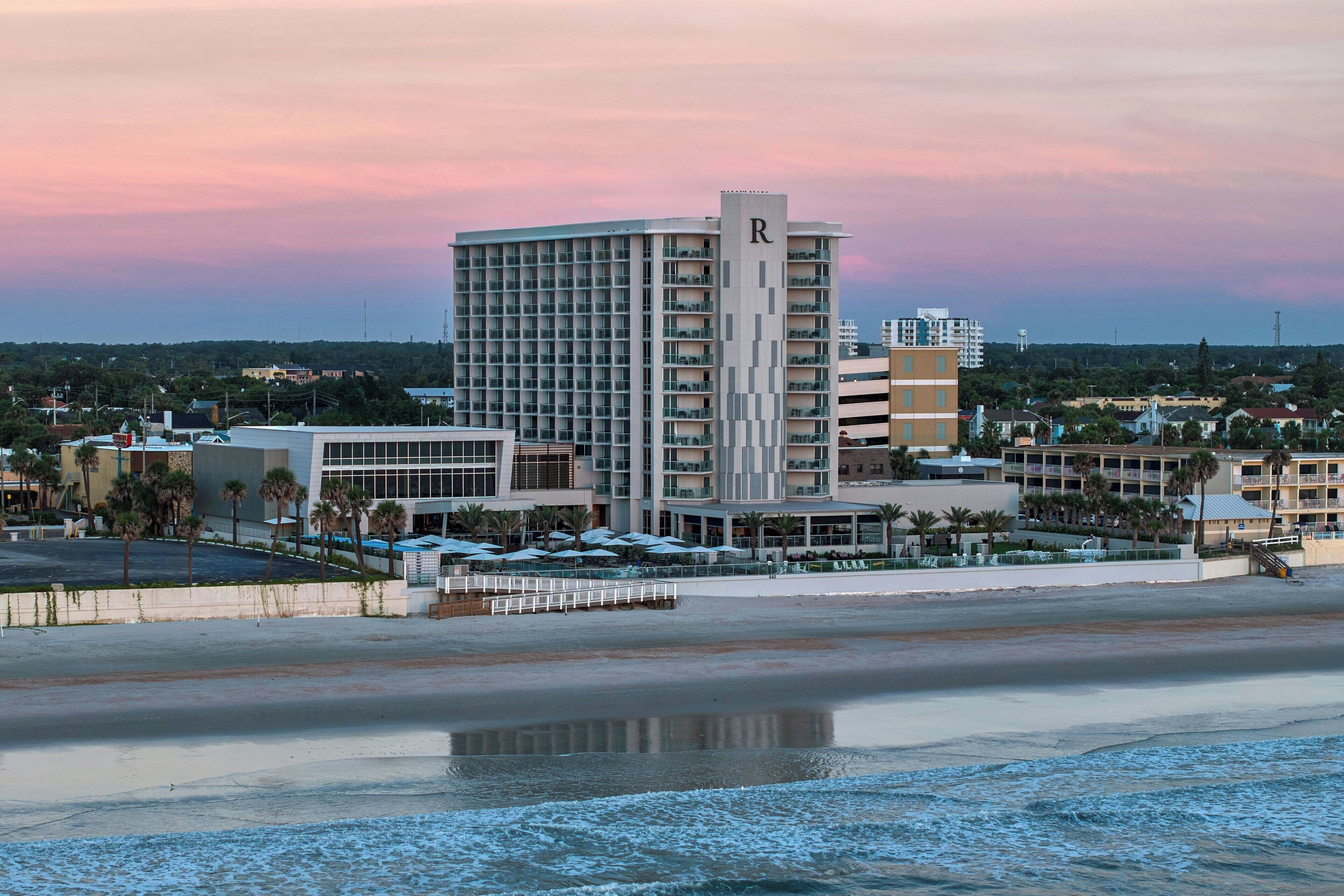 A hotel with a prominent 'R' on the building, a beach in the foreground, and a sunset sky.
