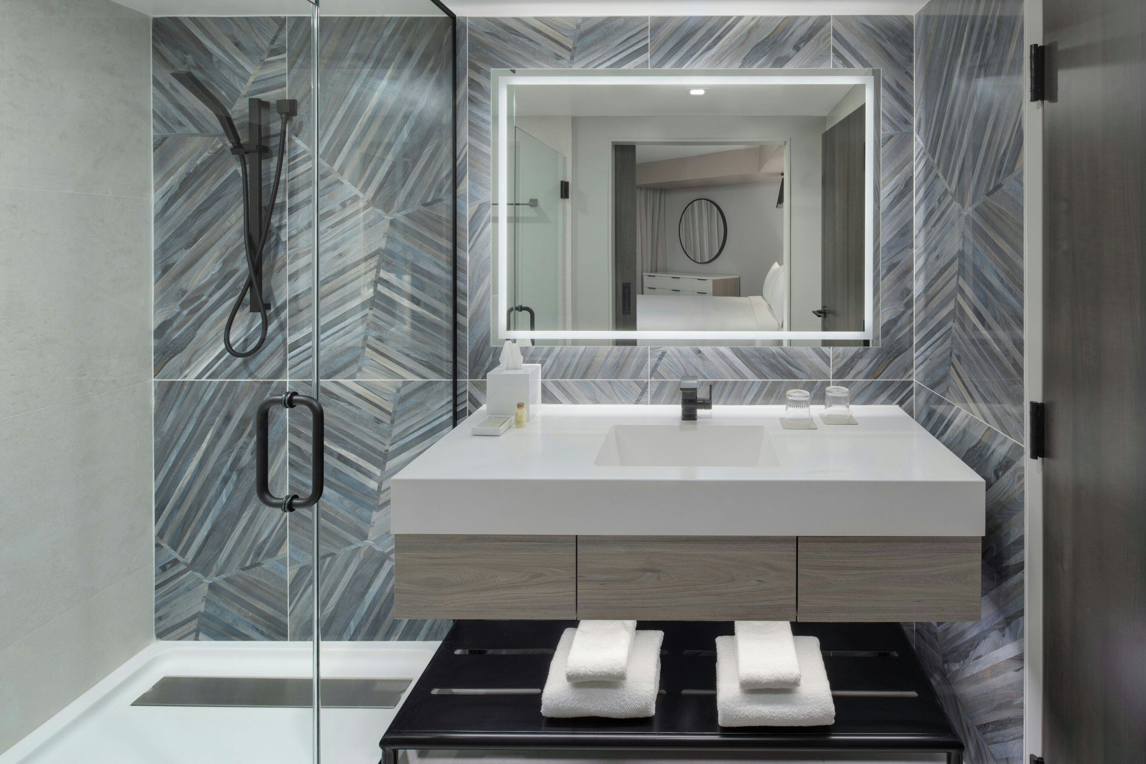 A modern bathroom with a glass shower enclosure, a white sink, and a mirror above it.