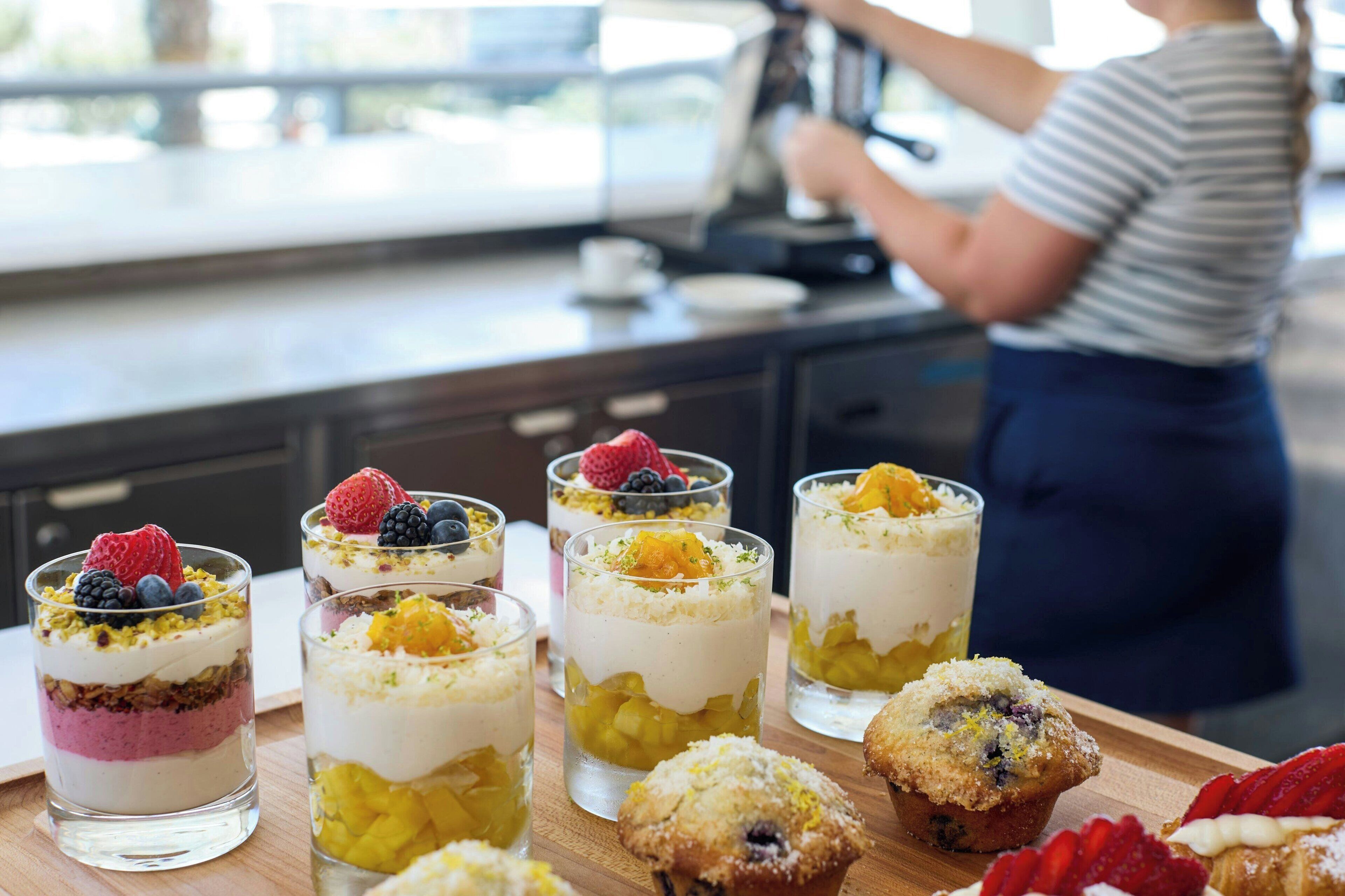 A dessert display with layered parfaits and muffins on a wooden board.