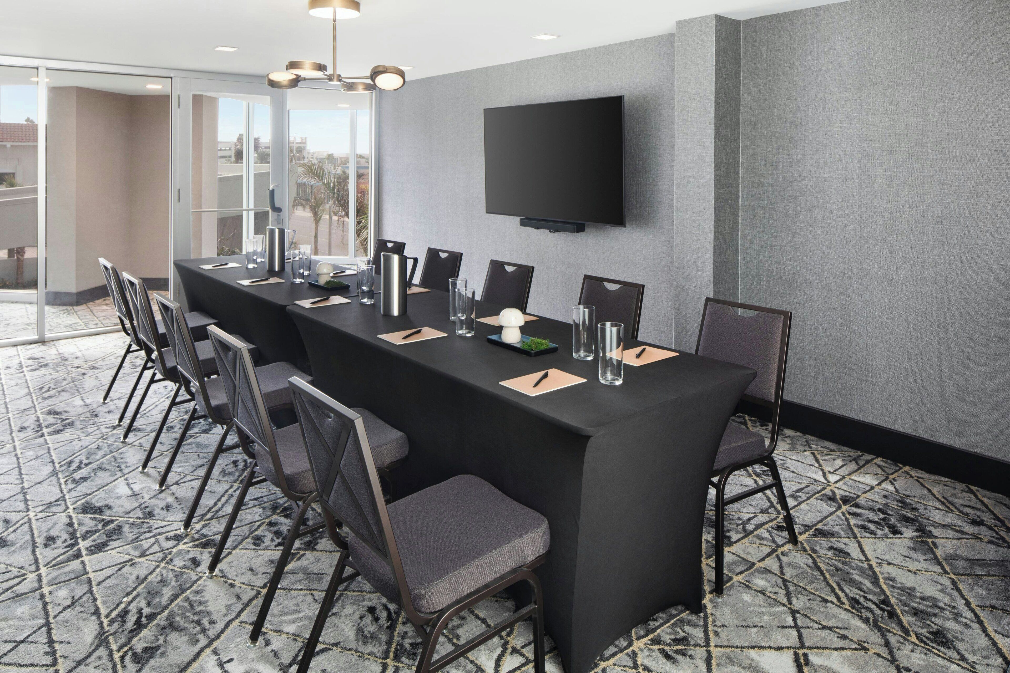 A conference room with a long table, chairs, a flat-screen TV, and a patterned carpet.