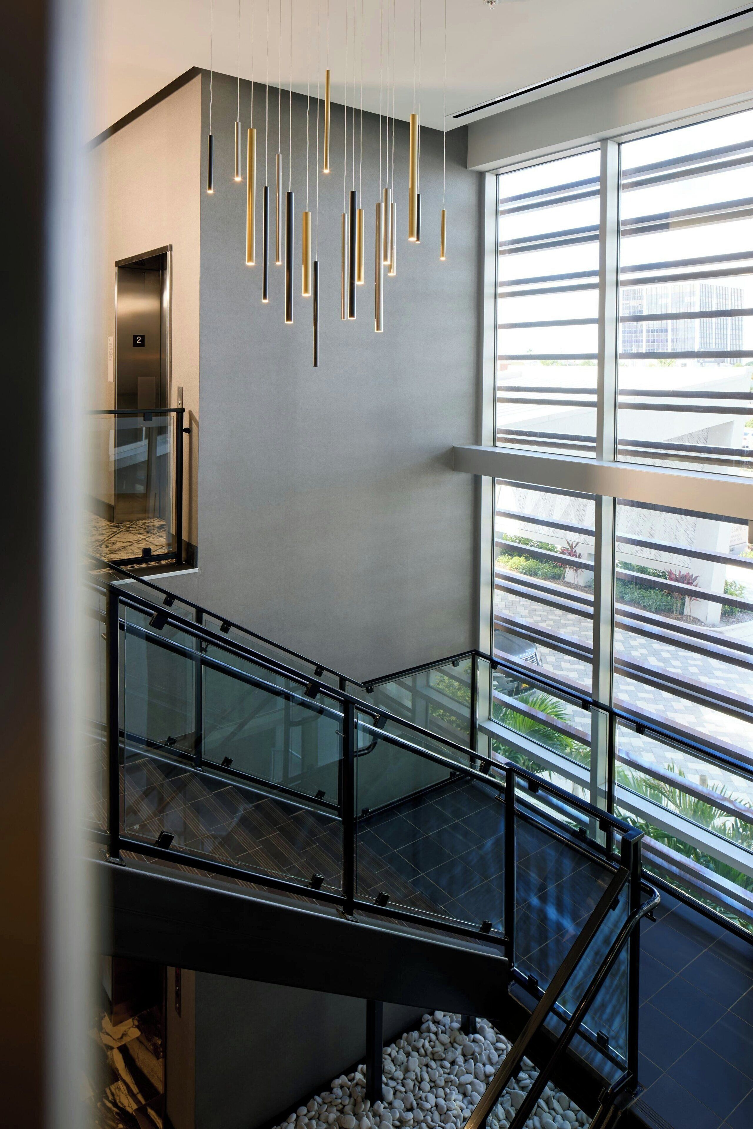 A modern interior with a glass railing, a hanging light fixture, and a view through large windows.