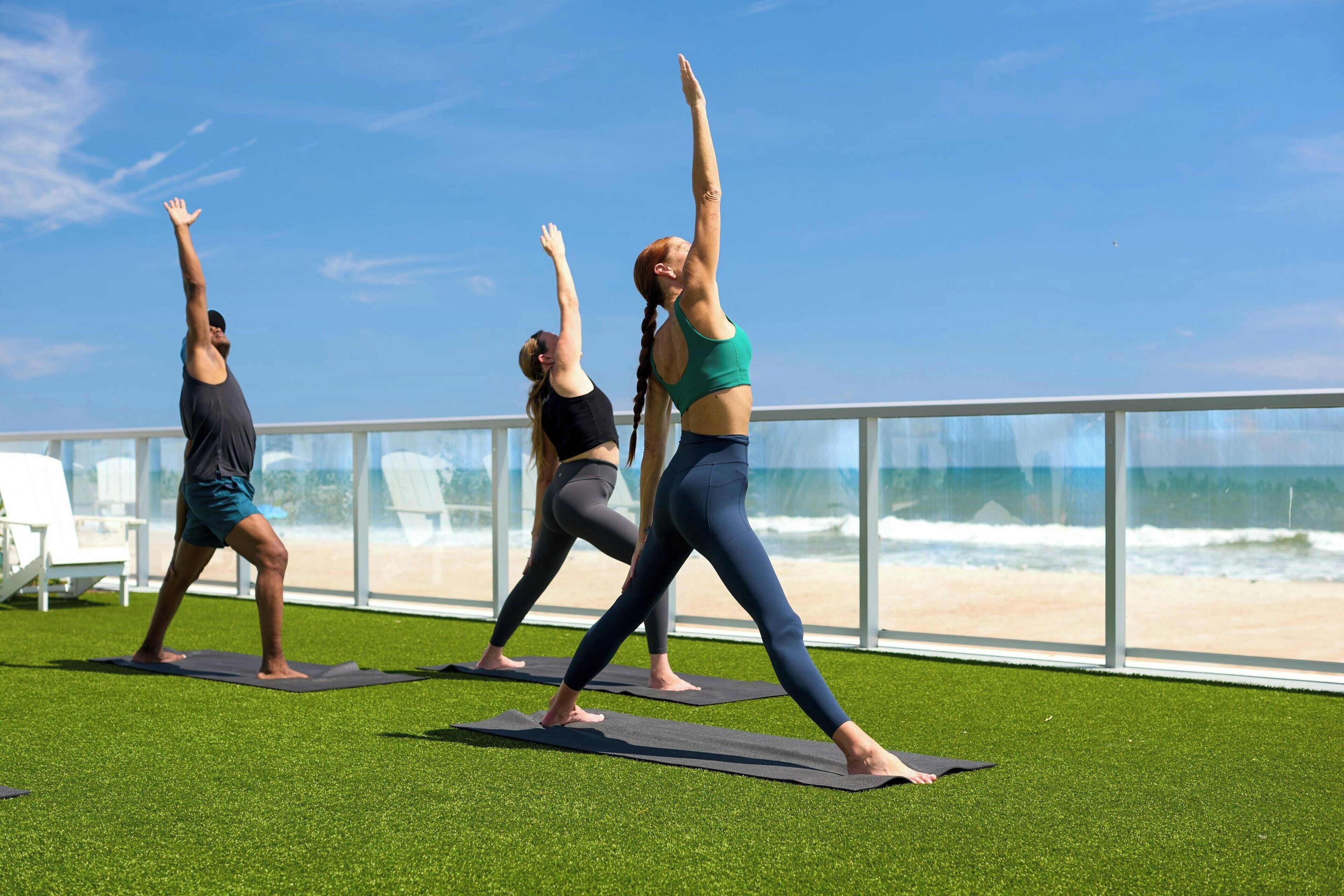 Three people doing yoga on a deck with a view of the beach.