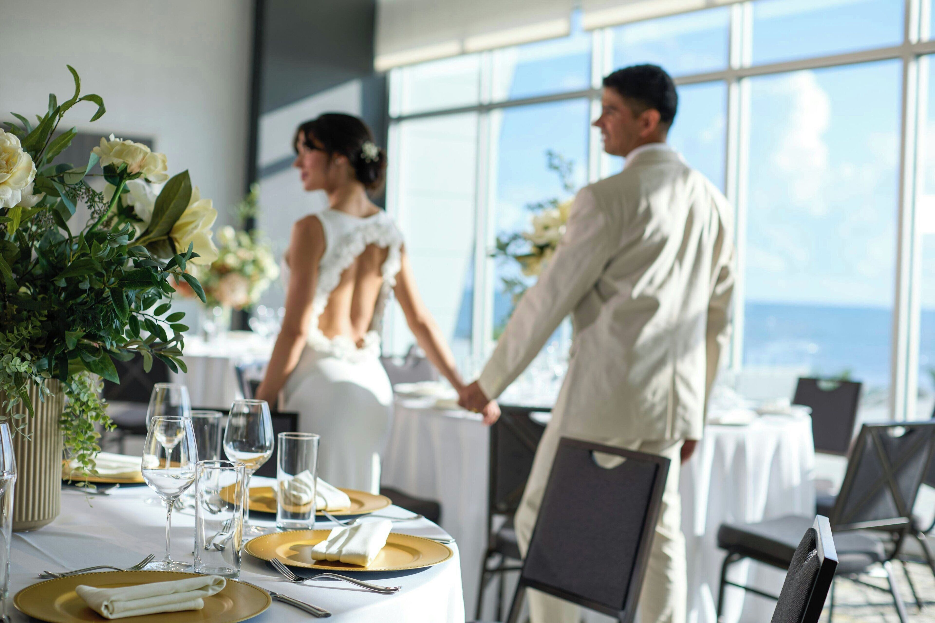 Una mesa de recepción de boda con manteles blancos, platos dorados y blancos, y cristalería transparente.