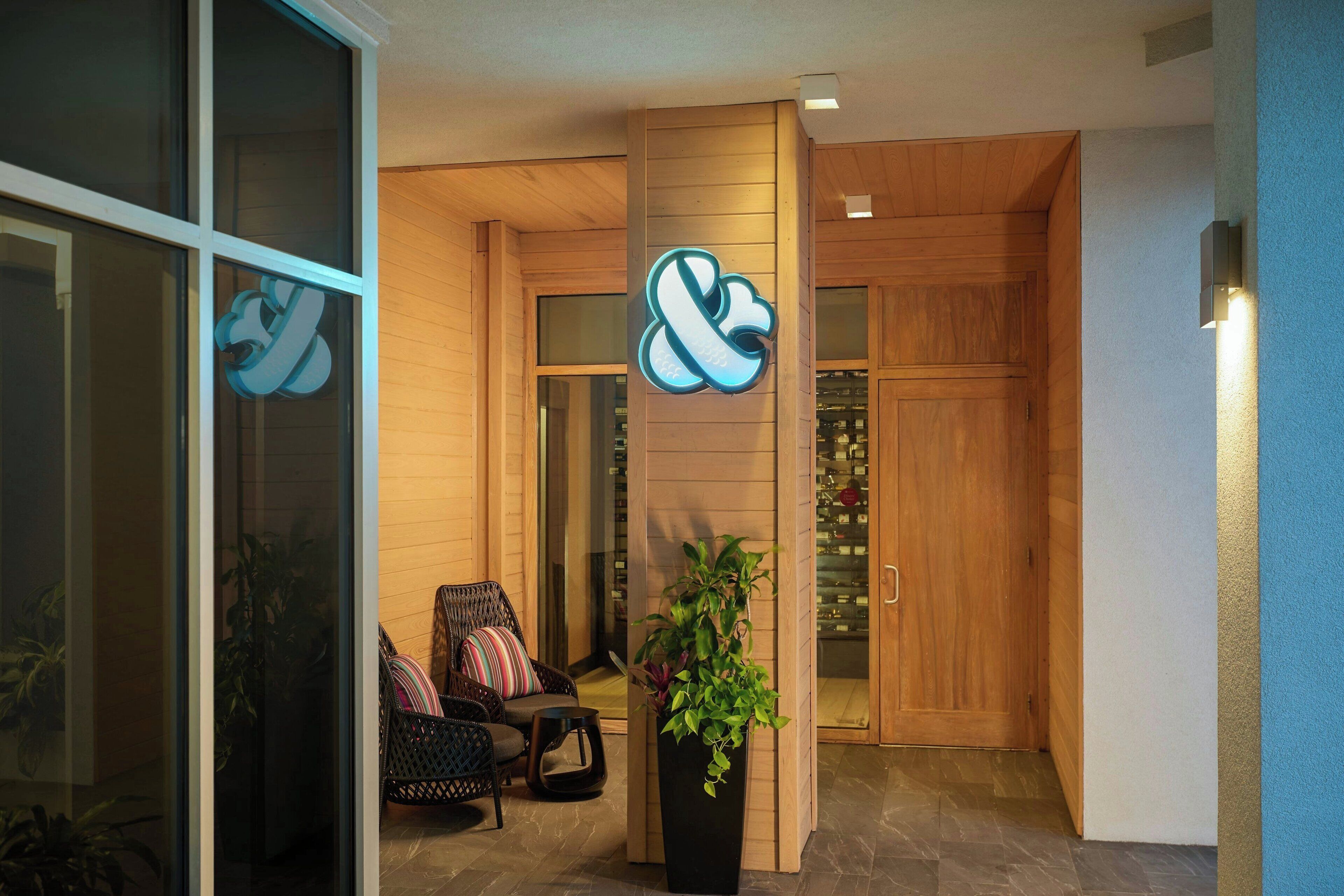 A reception area with a wooden door, a potted plant, and a seating area with a wicker chair and cushions.