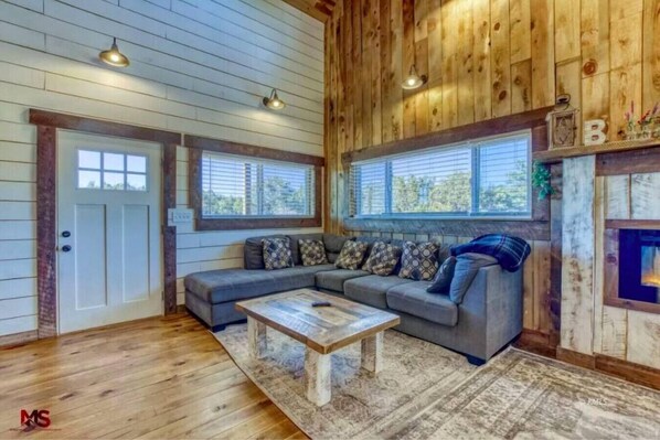 A cozy living room with a wooden ceiling, a gray sectional sofa, a wooden coffee table, and a fireplace.