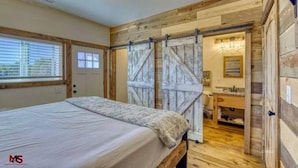 Une chambre à coucher avec un lit, des murs en bois, une porte coulissante de style grange et une salle de bain avec un lavabo et un miroir.