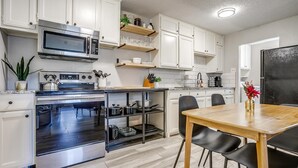 A modern kitchen with white cabinets, a built-in oven, a microwave, and a wooden dining table with black chairs.