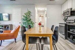 Eine moderne Küche mit Essbereich, ausgestattet mit einem Holztisch, schwarzen Stühlen und einem an der Wand montierten Fernseher.