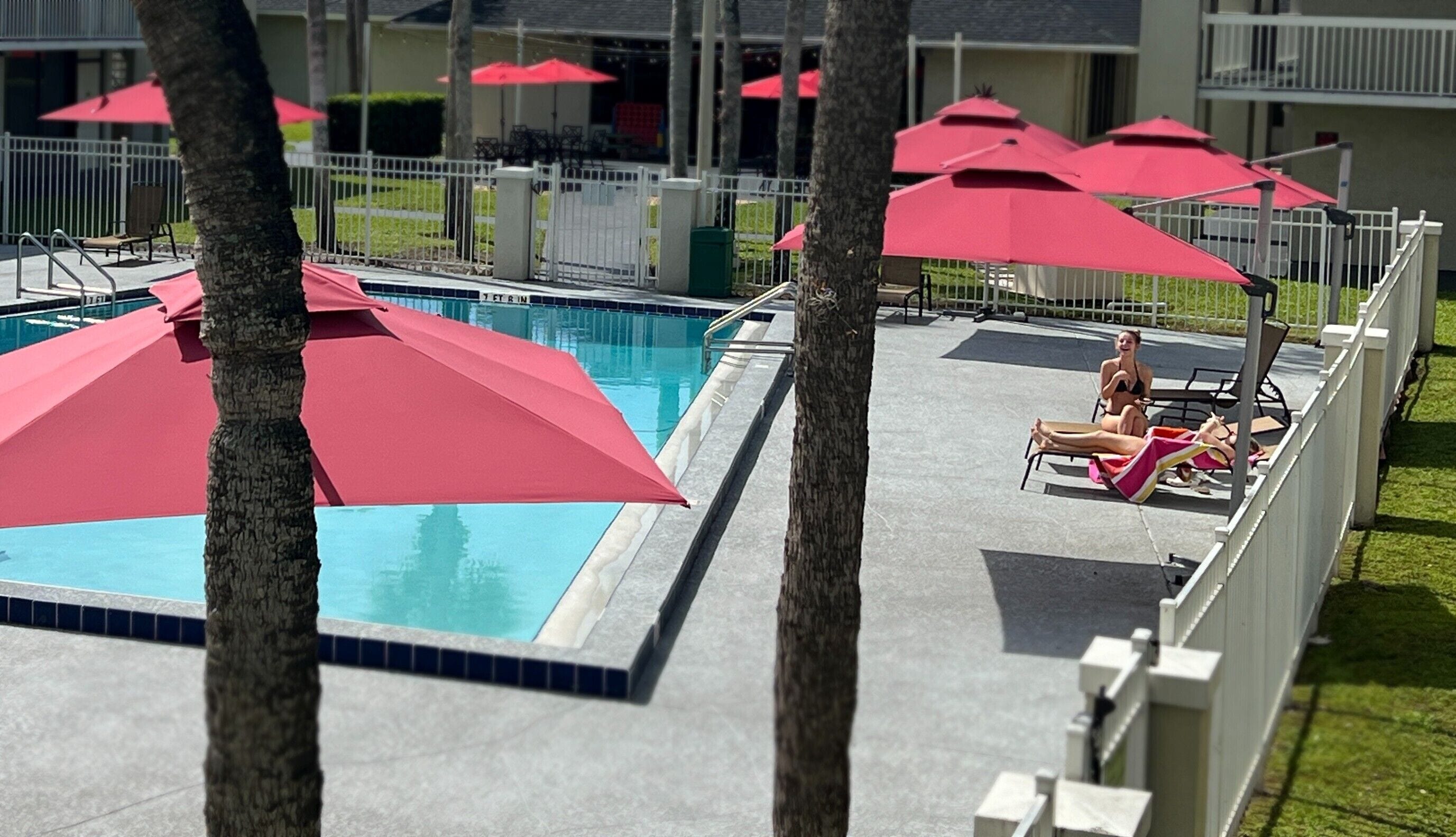 Uma área de piscina com vários guarda-sóis vermelhos e espreguiçadeiras.