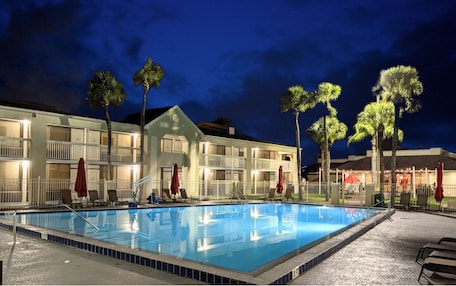 A hotel with a swimming pool, multiple balconies, and palm trees.