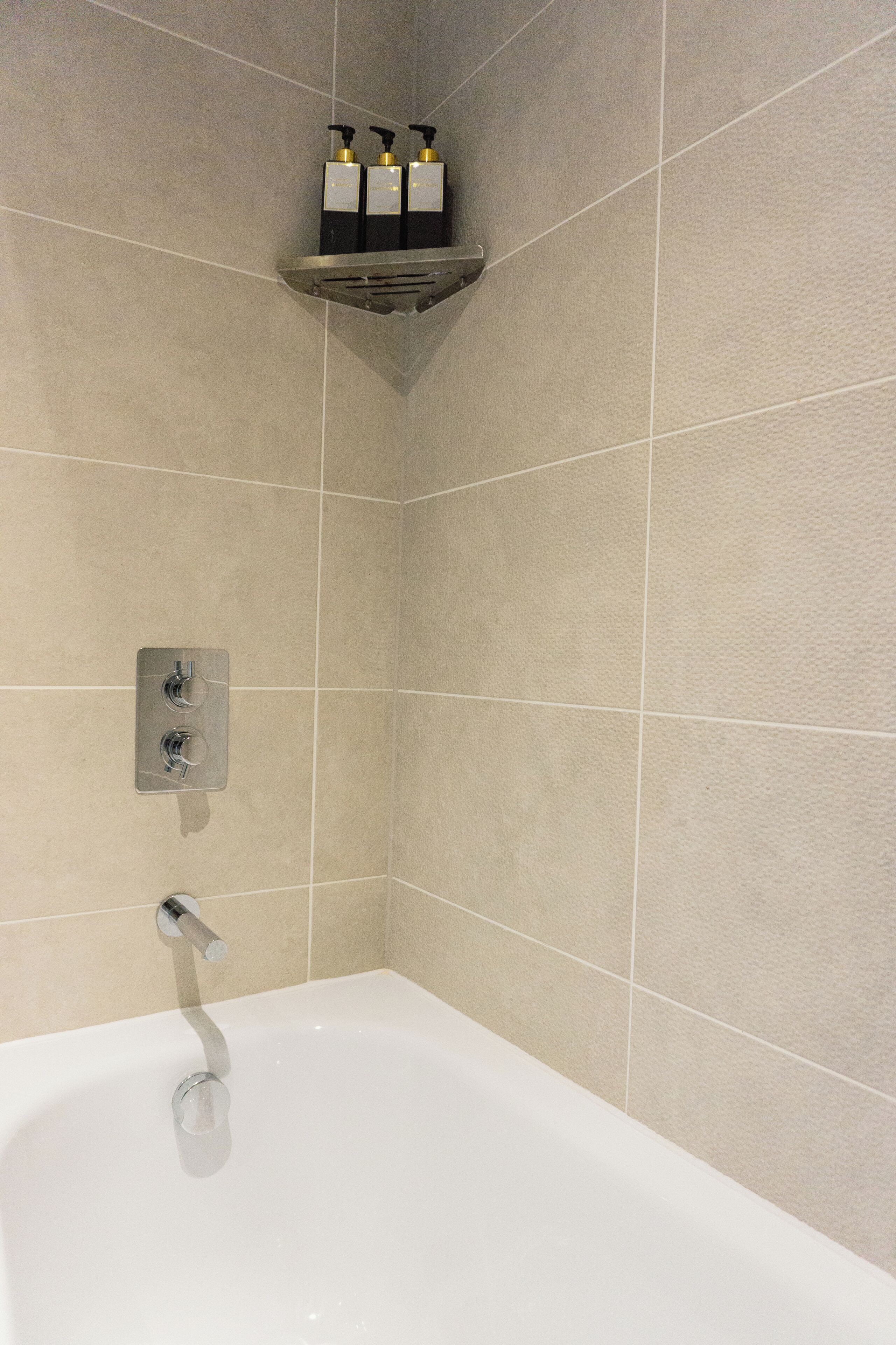 Een badkamer met een bad, een douchekop en een plank met toiletartikelen.