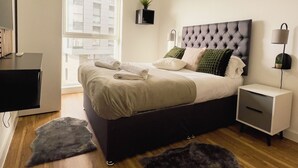 Un dormitorio moderno con una cama grande, mesitas de noche, un escritorio y un ventanal con vistas a la ciudad.