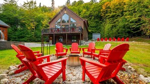 Eine Lodge mit einer Terrasse, roten Adirondack-Stühlen und einer Feuerstelle.