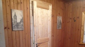 Una habitación con paneles de madera, una puerta de madera, un ventanal pequeño y dos cuadros en las paredes.