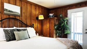 A bedroom with a wooden paneled wall, a bed with white bedding, a yellow lamp, and a potted plant.