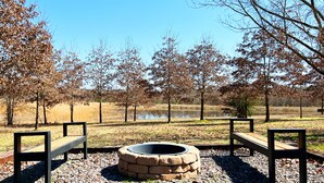 A park with two wooden benches and a stone fire pit.