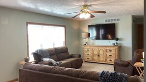 A living room with a ceiling fan, a flat-screen TV, and a large window.