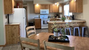 A modern kitchen with wooden cabinets, a central island, and a dining area with chairs.