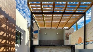 A covered outdoor seating area with a wooden pergola, stone walls, and a view of the sky. - Casa del Mural SAN Carlos (Guaymas)