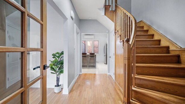 A hallway with wooden flooring, a potted plant, and a staircase with wooden railings. - Luxurious House Big Terrace | Sleeps 16 | 3bath (Montréal)