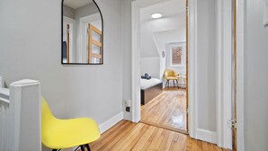 A hallway with a yellow chair, a mirror, and a door leading to a bedroom with a bed and a chair. - Luxurious House Big Terrace | Sleeps 16 | 3bath (Montréal)