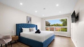 Un dormitorio con una cama grande, una silla, una mesita de noche, una ventana con vistas y un televisor montado.