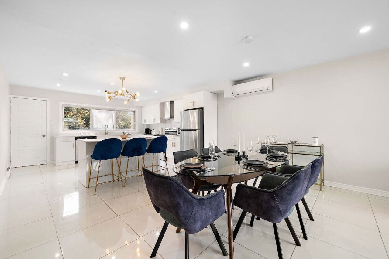 A modern kitchen with white cabinets, a stainless steel refrigerator, and a dining area with a glass table and blue chairs.