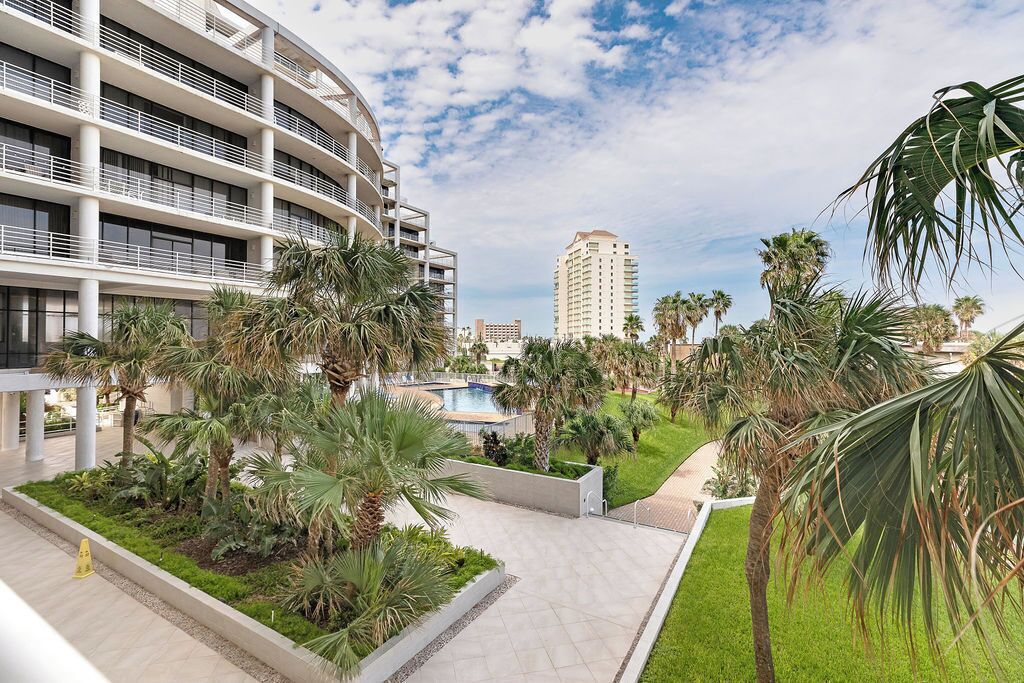 A modern hotel with a pool, palm trees, and a clear sky.