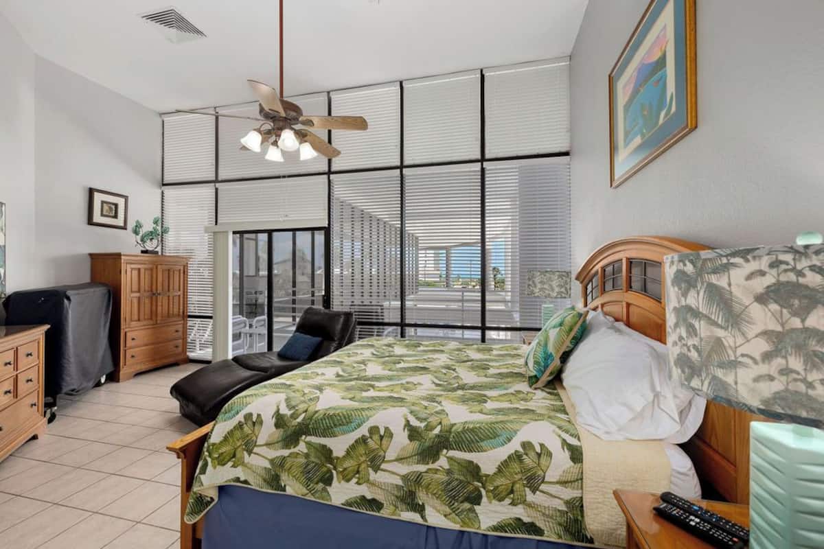 A bedroom with a bed, a desk, a chair, a wardrobe, and a ceiling fan.