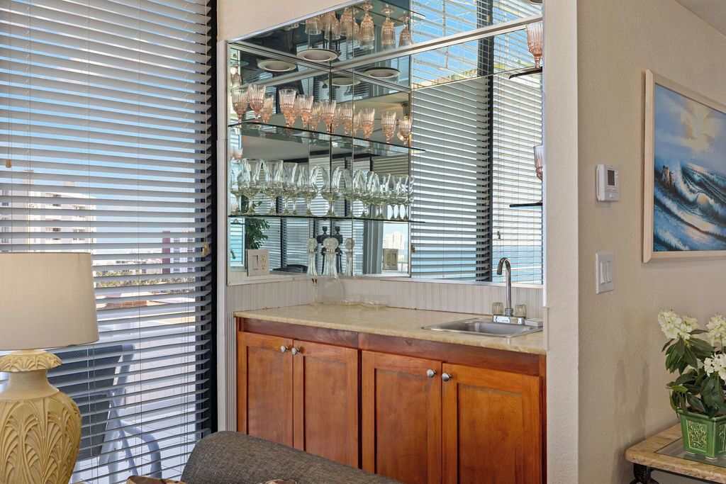 A kitchen with wooden cabinets, a countertop, a sink, and a glass display case with various glassware.