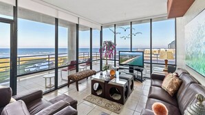 A spacious balcony with a view of the ocean, furnished with a sofa, a coffee table, and a TV. - Sunchase IV by South Padre Resort Rental (South Padre Island)