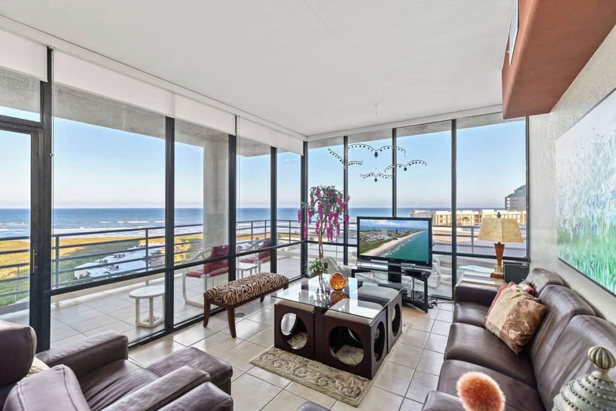 A spacious balcony with a view of the ocean, furnished with a sofa, a coffee table, and a TV.