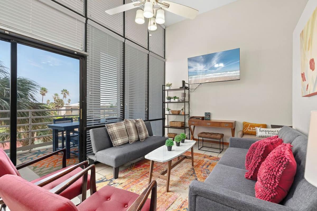 A modern living room with a grey sofa, a red armchair, and a coffee table. There is a bookshelf with decorative items and a painting on the wall.