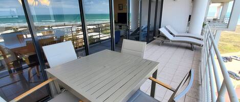 Un balcon avec une table et des chaises, offrant une vue sur la plage et l’océan.