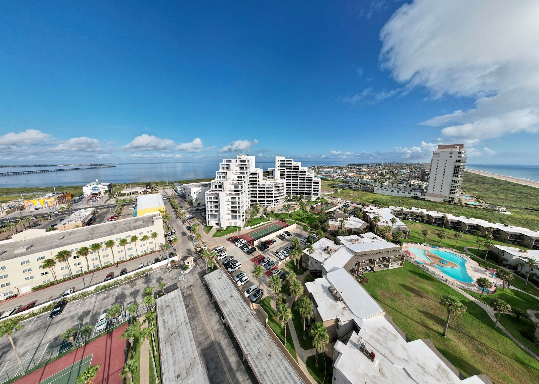 A coastal hotel complex with multiple buildings, a parking area, and a swimming pool.