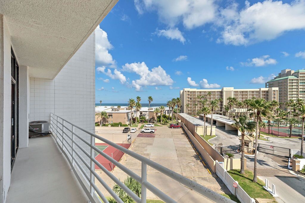 A hotel balcony with a view of a parking area, palm trees, and buildings in the background.