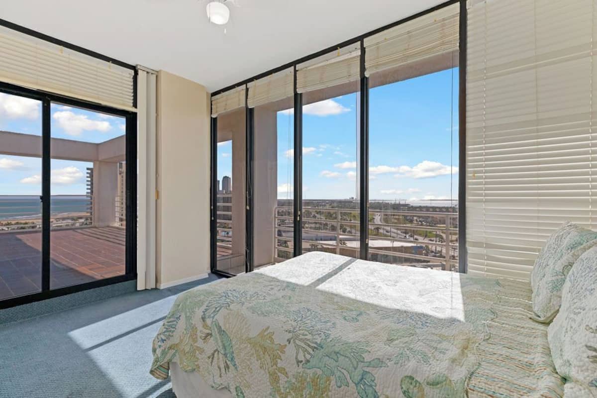 A spacious bedroom with large windows, a balcony, and a view of the cityscape.