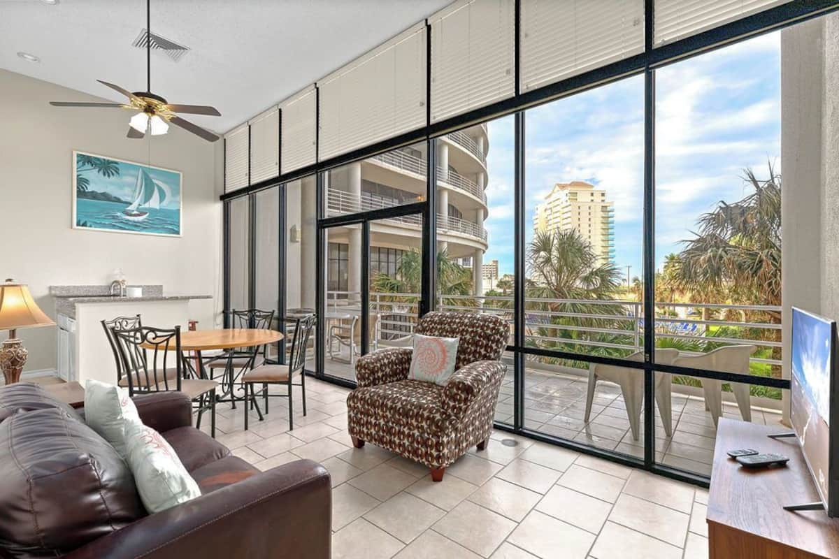 A spacious living area with a large window, a ceiling fan, a dining set, and a sofa.