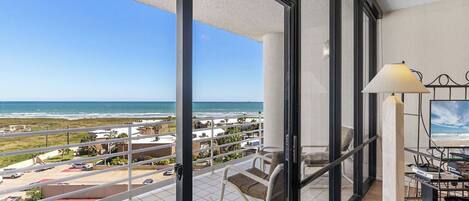 A balcony with a view of the ocean, a chair, a lamp, and a table.
