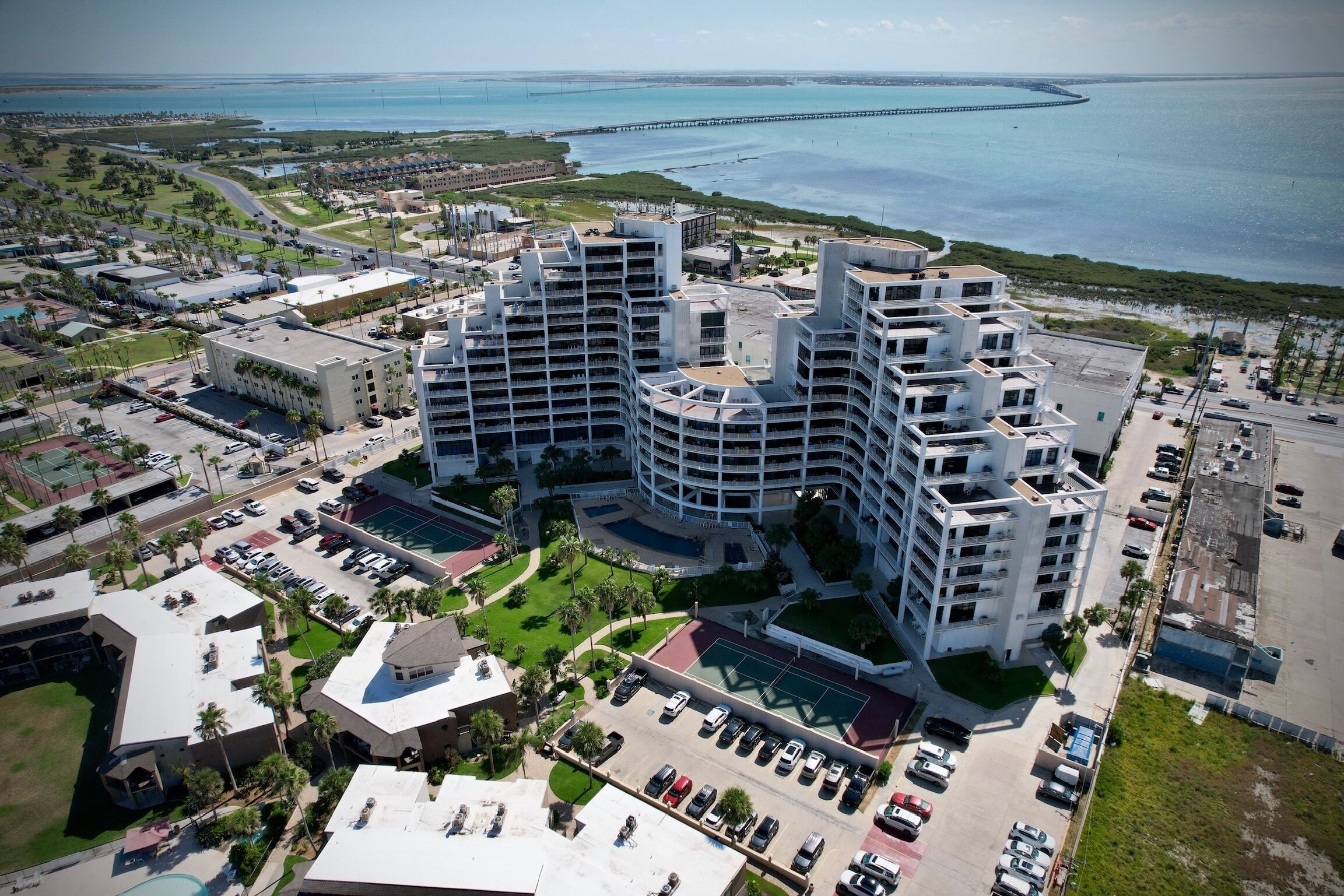 A high-rise hotel with multiple balconies, a swimming pool, and a view of the ocean and a pier.