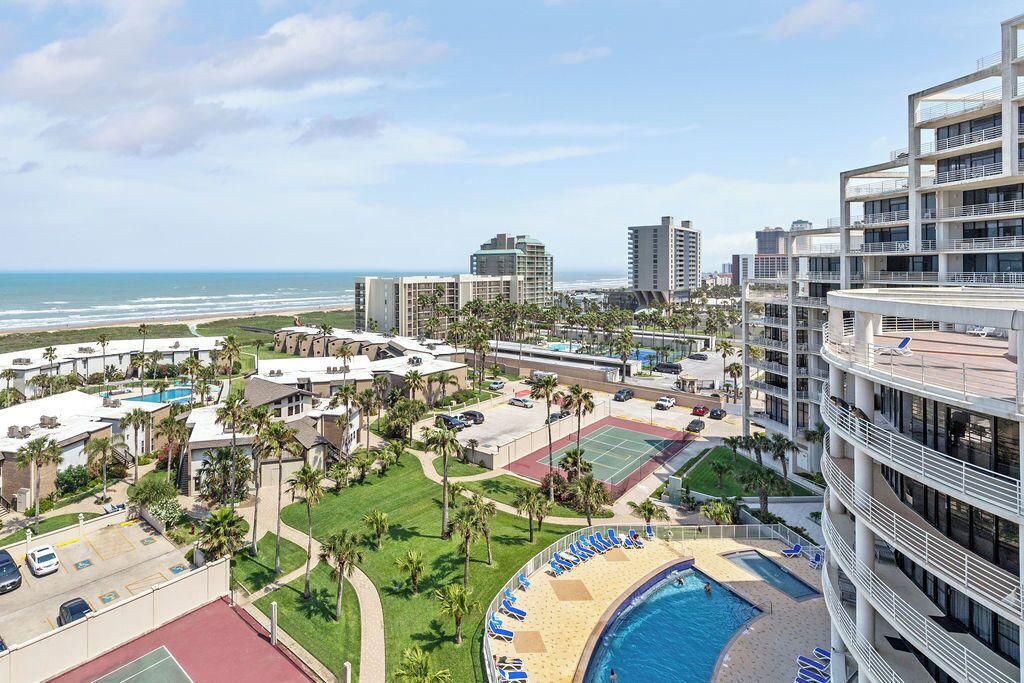 A hotel with a pool, tennis courts, and a view of the beach.