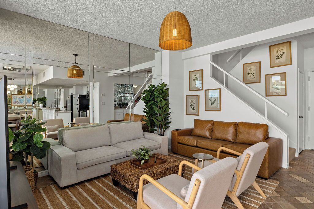 Ein modernes Wohnzimmer mit einer Couch, Sesseln, einem Couchtisch und einer Treppe mit gerahmten Bildern.