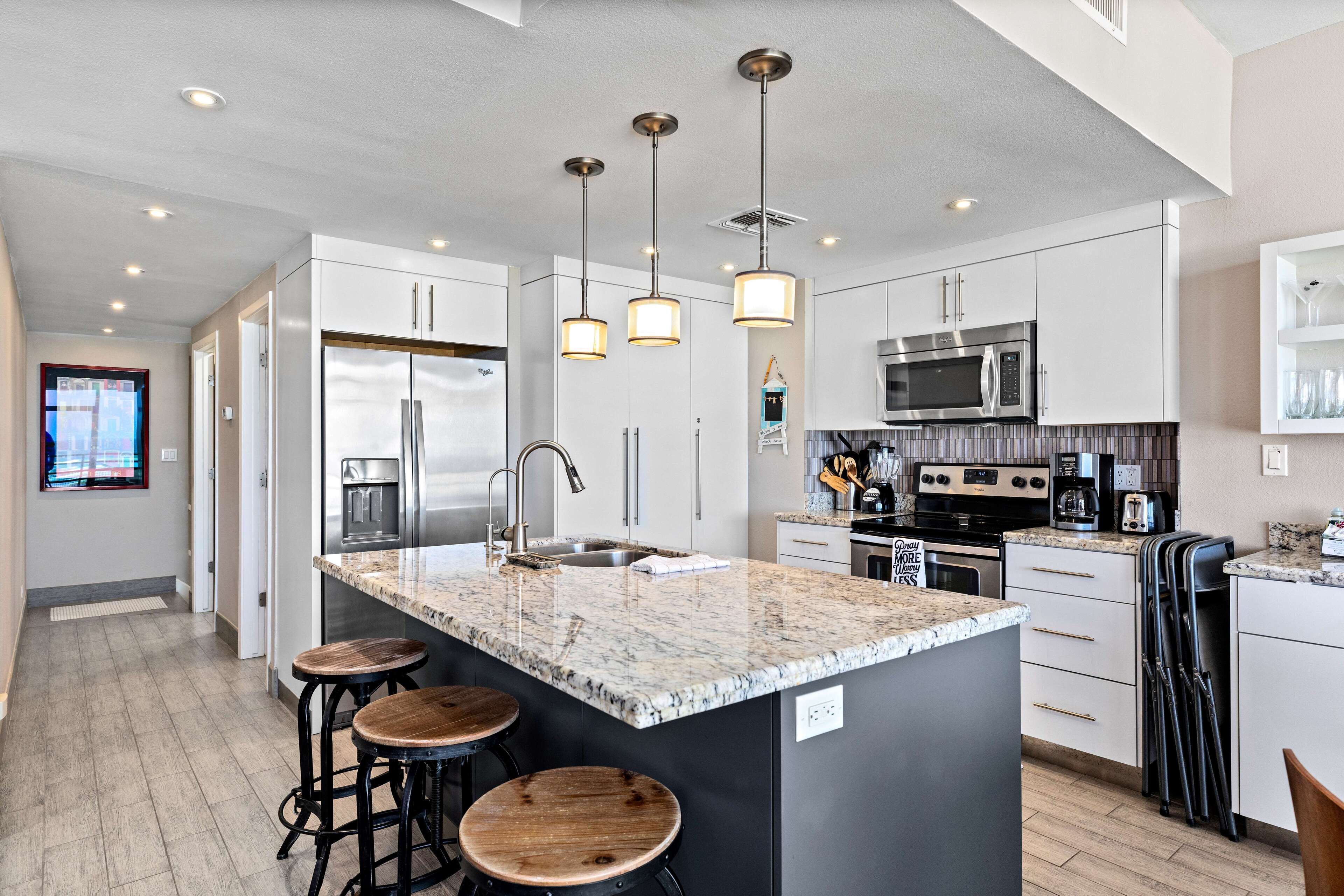 A modern kitchen with white cabinets, a granite countertop, stainless steel appliances, and a central island with stools.