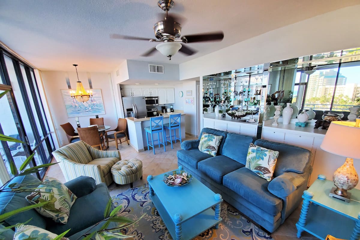 A modern living room with a blue sofa, a coffee table, and a dining area with a kitchen in the background.