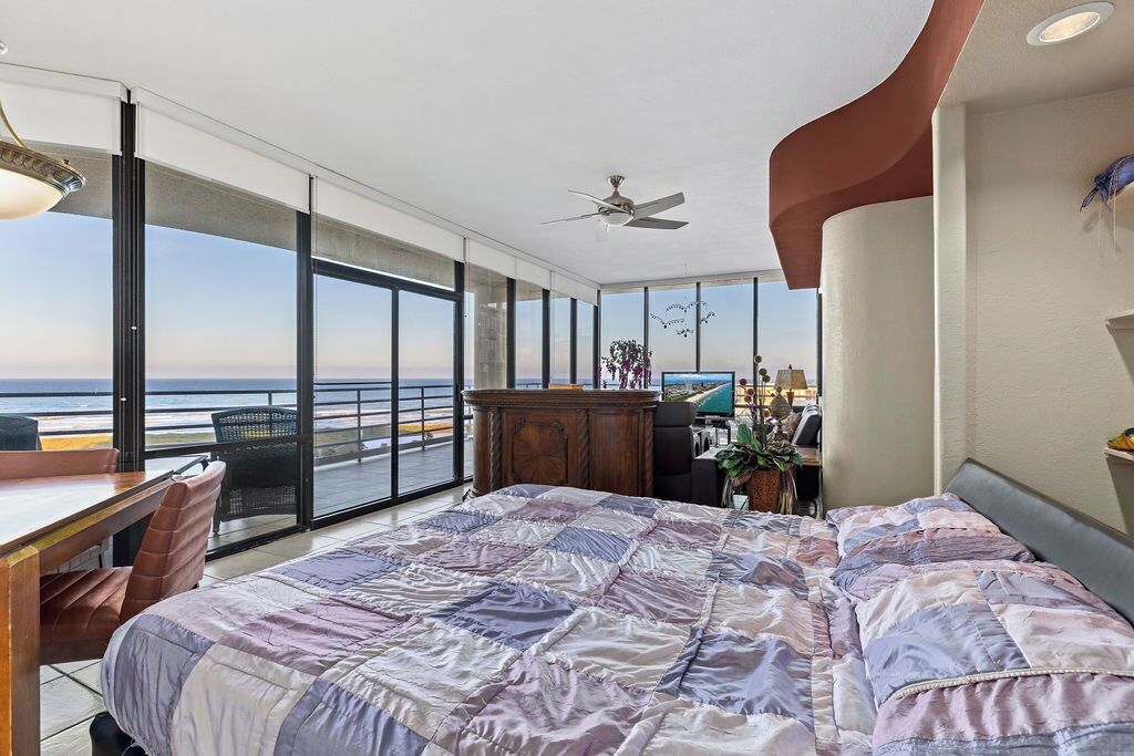 A modern bedroom with a large bed, a desk, and a view of the ocean.