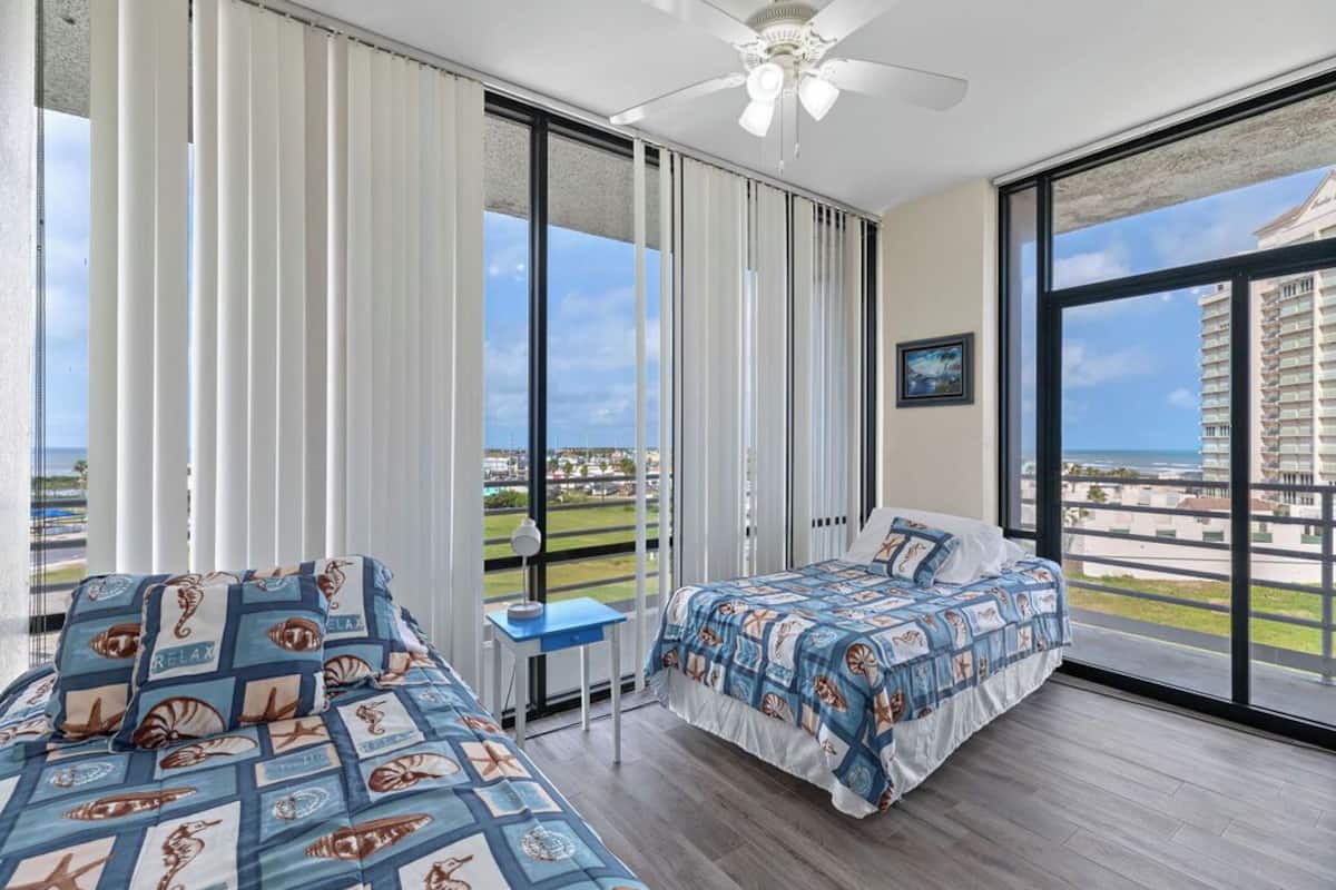 A bedroom with a bed, a desk, and a view of the ocean.