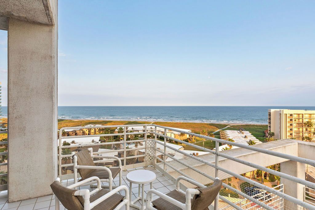 A balcony with a view of the ocean, white outdoor furniture, and a tiled floor.