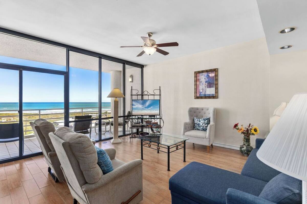 A spacious living room with a large glass door leading to a balcony overlooking the ocean.